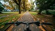 © Kate Mova - A view from the handlebars of a bicycle riding down a tree-lined path covered in autumn leaves. The scene captures the essence of fall and outdoor activity.