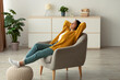 © Prostock-studio - A relaxed Arab woman is sitting in a comfortable armchair with her hands behind her head and eyes closed. She enjoys her weekend, finding peace in her home environment.