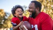 © Andrii - happy portrait of an African American father and his young son in red jerseys, laughing together outdoors. Use for family bonding, sports coaching, childhood joy, parenting