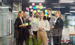© Studio Romantic - Motivated young team happy planning development discussing creative startup ideas on sticky papers, employees looking at stickers, successful workers brainstorming behind modern glass office wall