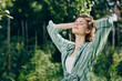 © SHOTPRIME STUDIO - Woman outdoors, eyes closed, basking in sunlight with a striped green shirt, standing in a lush park, feeling calm and free.