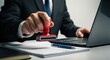 © Razaul Karim - A businessman in a suit stamps a document while working on a laptop, symbolizing approval and official business processes