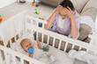 © Pixel-Shot - Young mother with her baby in crib suffering from postnatal depression at home
