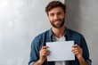 © Iryna - Smiling young caucasian male holding blank cardboard against gray background