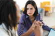 © Studio Marmellata - A serious young woman in a purple shirt listens attentively to her male colleague during a professional discussion. They are working together in a bright office environment.