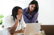 © Studio Marmellata - Two diverse colleagues collaborate on a project, reviewing content on a laptop screen. The man sits while the woman stands, both intently focused on their shared work.