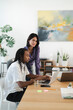 © Studio Marmellata - Diverse business professionals collaborate on a laptop in a modern office setting. The man works at the desk, and the woman stands, smiling. Effective teamwork and shared success.