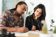 © Studio Marmellata - A diverse couple collaborates on a project at a bright table. The man writes on documents while the woman attentively observes, holding a pencil. They are focused on their work.
