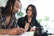 © Studio Marmellata - Two diverse young professionals collaborate on a project at a desk. The man writes while the woman observes, holding a pencil. They are focused on their work.