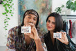 © Studio Marmellata - A diverse man and woman hold up instant photos of themselves, smiling directly at the camera. They share a happy moment indoors, surrounded by plants and a colorful backdrop.