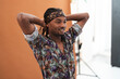 © Studio Marmellata - Young Black man with dreadlocks and a patterned headband smiles while posing with his hands behind his head in a studio setting. He wears a colorful shirt.