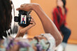 © Studio Marmellata - A photographer captures a portrait of a female model. The photographer holds a camera, and the model is visible on the camera's screen, wearing a red plaid shirt and blue jeans.