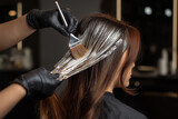 Hairdresser dyeing woman’s hair using brush, professional salon setting