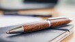 © Sergey - close up of a polished wooden pen resting on a notebook, shallow depth of field, clean workstation with soft daylight, elegant professional mood
