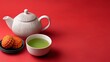 © Nataliia_Trushchenko - A teapot and a bowl of green tea sit on a red table. The teapot is white and has a black handle. There are also some red and yellow pastries on the table