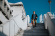 © qunica.com - A young man in casual clothes descends concrete stairs outdoors, carrying a red bag. The urban backdrop and blue sky convey everyday commute, independence, and urban exploration.