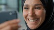 © Yuliia - Portrait happy arabian business woman in hijab smiling looking in phone laughing smile Muslim businesswoman female girl with smartphone app carefree emotional joyful look in mobile smartphone email