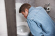 © New Africa - Young man suffering from nausea over toilet bowl in bathroom, back view