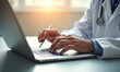 © miss irine - Doctor with stethoscope works on laptop. Physician types on computer keyboard at desk. Healthcare pro researches info online. Medical worker uses tech for patient care.