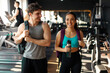 © Home-stock - Man and woman walking through gym, smiling and chatting, carrying backpacks and woman holding water bottle, dressed in workout gear