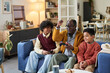 © Mediaphotos - Black senior man sitting on sofa playing video game with two Black boys, one teenager and one child, all holding controllers and focusing on television screen in modern living room