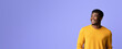 © Prostock-studio - A man with a joyful expression stands against a purple wall. He is wearing a bright yellow sweater and appears happy, enjoying a light-hearted moment. The setting is bright and uplifting.