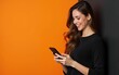 © ye - Photo of An elegant young woman in her 20s with long wavy hair, happy smiling while using an mobile phone on a orange and black background with copy space for text or product. Web banner.