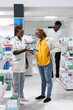 © DC Studio - African american expert helps woman with a muscular injury problem, recommending painkillers and vitamins to cure backache. Female client with lower back muscle pain at drugstore.
