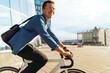 © muse studio - Young man biking in urban area with modern buildings