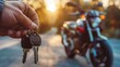 © ds17 - A hand holds motorcycle keys in front of a parked motorcycle during sunset. The scene captures a moment of anticipation and adventure.