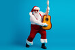 © deagreez - Santa with guitar in bright blue studio wearing red suit with white fur trim sunglass creates festive holiday mood as he performs a cheerful tune