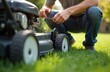 © Pete - Man crouches on grass, checks oil level in lawn mower engine with dipstick. Male gardener maintains garden equipment. Person in jeans and t-shirt services motor lawn mower in backyard on a sunny day.
