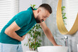 © New Africa - Man suffering from stomach ache and nausea over sink in bathroom