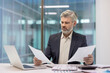 © Liubomir - Mature businessman studying important paperwork, comparing financial reports and data analysis, making focused decisions while working in a modern corporate office