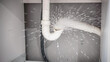 © Varos - Emergency plumbing problem showing a burst white plastic pipe under a sink, with water spraying out, leading to potential flooding and damage