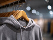 © Daria - Soft gray hooded sweatshirt hanging on wooden hanger with blurred background in modern clothing store interior under warm lighting
