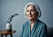 © OlehStock - Studio portrait elderly woman silver hair teal blouse wooden table ceramic vase eucalyptus cool-neutral lighting facial lines skin texture longevity