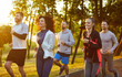 © Studio Romantic - Group of runners jogging together with smiles through summer park in morning outdoor cardio workout. Marathon and race of happy fit people on track, athletes exercising, training energy and endurance