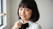 © Running opossum - young asian girl smiling confidently inside a bright room wearing a school uniform with a bow tie