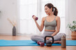 © Kiattisak - Young Asian woman exercising at home with dumbbells and kettlebell, sitting on yoga mat in activewear. Healthy lifestyle, indoor workout, strength training and wellness concept.