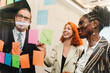 © artitwpd - Diverse professionals smiling and collaborating during a brainstorming session, using colorful sticky notes on a glass wall in a bright modern office, showing teamwork and creative planning.