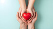 © Ahmed - Show your love and compassion with a heart being held by adult and child hands on a soft blue background