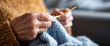 © perfectlab - Close-up of elderly hands knitting a blue woolen garment with wooden needles in a cozy indoor setting