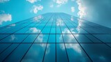 Low angle view of a glass skyscraper reflecting the clouds and blue sky on a bright sunny day