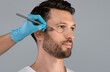 © Prostock-studio - Handsome man with pencil marks under eyes for cosmetic surgery or correction, ready for operation. Plastic Surgery concept. Plastic surgeon applying marks on man face before surgery, grey background