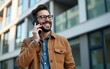 © Sophia - Smiling male freelancer in eyeglasses is talking phone standing on coworking building background. High quality