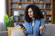 © Liubomir - Woman feeling frustrated and confused while trying to make an online payment with a credit card and smartphone, indicating a problem or declined transaction