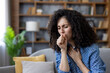© Liubomir - Woman with curly hair suffering from a painful cough, feeling unwell due to a cold, flu, allergy, or other respiratory illness while resting on a sofa in her home
