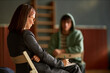 © TrueFrame Collective - Caucasian woman writing on clipboard while sitting across from teenage boy in hoodie during psychology session, focusing on student counseling and mental health support