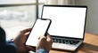 © Gerlot - Cell phone and laptop white screen mockup,blank screen while working on laptop at office,Woman hand holding mobile phone Business woman using smartphon